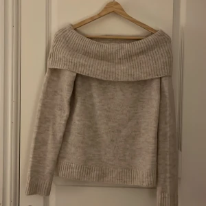 Beige offshoulder stickad tröja - Mysig beige stickad tröja med offshoulder-design. Perfekt för kyliga dagar med sin ribbade kant och långa ärmar. En stilren och bekväm tröja som passar till många tillfällen.