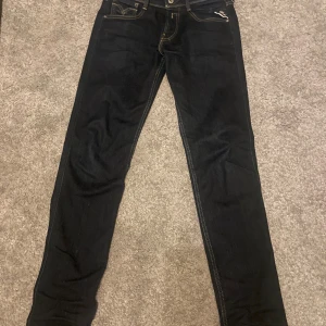 Mörkblå jeans från Replay - Snygga svarta jeans från Replay med klassisk femficksdesign och kontrastsömmar. De har en knappgylf och bälteshällor för extra stil. Perfekta för en cool och avslappnad look.