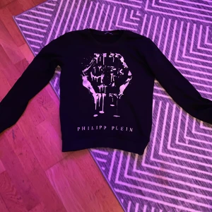 Svart tröja från Philipp Plein - Snygg svart tröja från Philipp Plein med ett coolt tryck av en dödskalle på framsidan. Tröjan har långa ärmar och en rund halsringning. Perfekt för en trendig look.