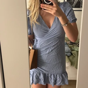 Ljusblå omlottklänning från Gina Tricot - Säljer en söt ljusblå omlottklänning från Gina Tricot. Klänningen har korta puffärmar och en volangdetalj vid fållen. Perfekt för sommarens alla tillfällen. 💙