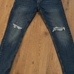 Blå jeans med slitningar - Snygga blå jeans med slitningar på knäna för en trendig look med en slim passform. De har en klassisk femficksdesign och en bekväm passform. Perfekta för en avslappnad stil