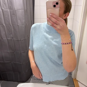 Ljusblå stickad tröja - Säljer en ljusblå stickad tröja med korta ärmar och ribbade kanter. Perfekt för en stilren och bekväm look. Passar bra till både jeans och kjol.