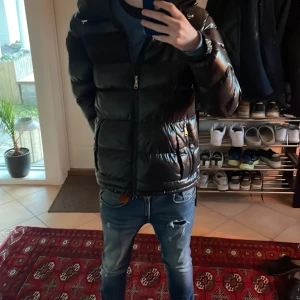 Svart pufferjacka från Alessandro zavetti - Säljer en snygg svart pufferjacka från Alessandro zavetti. Den är perfekt för kalla dagar med sin vadderade design och har en praktisk dragkedja framtill. Jackan har en huva och långa ärmar, vilket gör den idealisk för både höst och vinter. Den är i mycket bra skick!