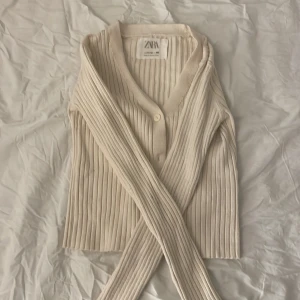 Beige ribbad kofta från Zara - Säljer en superfin beige ribbad kofta från Zara i storlek 152. Den har en v-ringad design med knappar framtill och är perfekt för både höst och vår. Koftan är i mycket bra skick och passar till alla tillfällen. Perfekt att ha över en t-shirt eller blus för en stilren look!