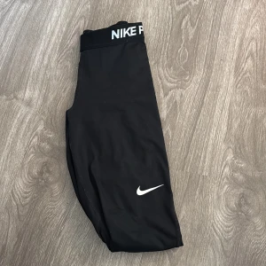Svarta leggings från Nike - Säljer ett par svarta leggings från Nike Pro. De är perfekta för träning med en tight passform och hög midja för extra stöd. Materialet är mjukt och stretchigt, vilket gör dem bekväma att bära under långa träningspass. Nike-loggan syns tydligt på benet och midjan.