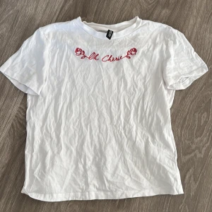 Vit t-shirt med röd text - Säljer en vit t-shirt från H&M med röd broderad text 'Oh Cherie' och rosor på bröstet. Den är kortärmad och i bomull.