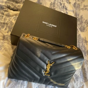 Svart quiltad väska från Saint Laurent - Säljer en elegant svart quiltad väska från Saint Laurent. Väskan har en lyxig känsla med guldfärgade kedjedetaljer och det ikoniska YSL-emblemet på framsidan. Perfekt för både vardag och fest! Kommer med originalförpackning. Både dust och låda. Skriv för fler bilder och eller frågor💕