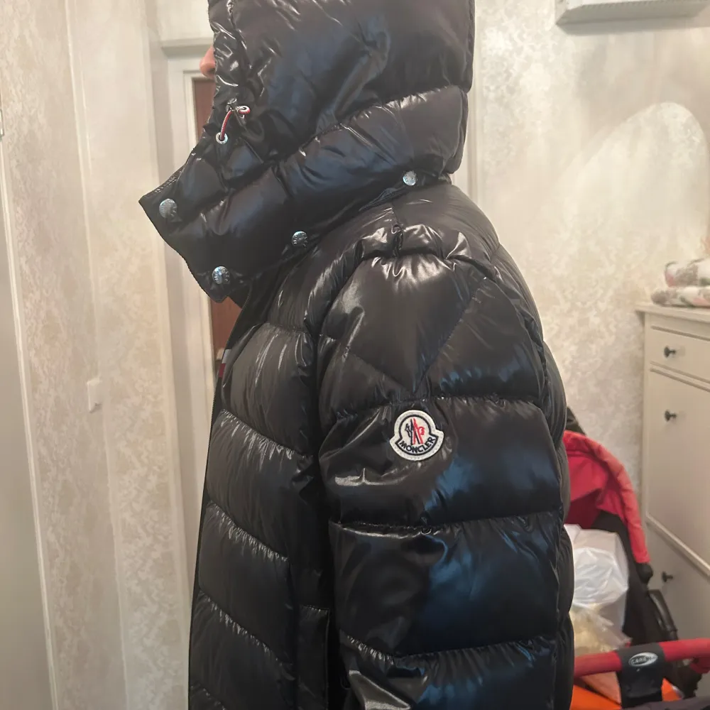 Säljer en snygg och varm svart dunjacka från Moncler i mycket bra skick. Jackan har en glansig finish och är perfekt för kalla vinterdagar. Den har en dragkedja framtill och en huva för extra skydd mot väder och vind. Passar perfekt för både vardag och festliga tillfällen.. Jackor.