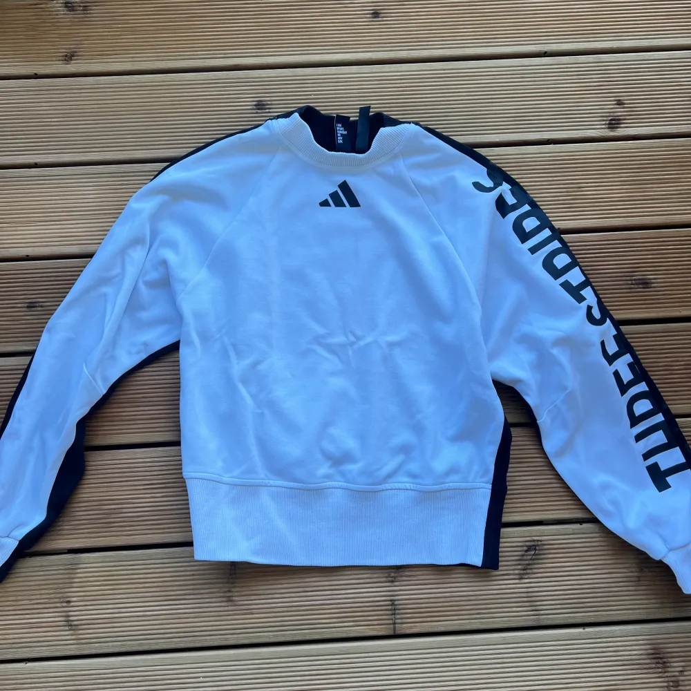 Säljer en snygg vit och svart tröja från Adidas. Den har långa ärmar och texten 'THREE STRIPES' längs ena ärmen. Perfekt för en sportig look eller chill vardagsstil. Tröjan är i bra skick och redo för nya äventyr!. Tröjor & Koftor.