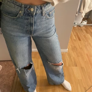 Blå jeans med slitningar - Säljer ett par snygga blå jeans med slitningar på knäna. De har en hög midja och en straight passform som ger en avslappnad look. Perfekta för en casual outfit och passar till alla årstider. De är i bra skick och redo för nya äventyr!