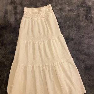 Vit långkjol från Gina Tricot - Säljer en superfin vit långkjol från Gina Tricot i storlek 146/152. Kjolen har en elastisk midja och är i ett luftigt material som ger en härlig volang-effekt. Perfekt för sommardagar eller festliga tillfällen! 🕊️Den ger så mycket svensk sommar vibe🌸. Jätte fin att styla med en off shoulder volang topp. Aldrig använd! 🥰