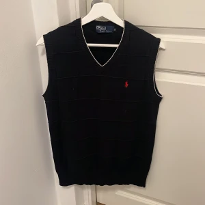 Svart stickad väst från Ralph Lauren - Storlek M men passar S. Säljer en snygg svart stickad väst från Ralph Lauren med V-ringning och röd broderad logga på bröstet. Perfekt för lager-på-lager under höst och vår. Västen har vita detaljer vid hals och ärmslut.