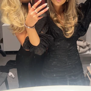 Svart klänning med detaljer  - Säljer denna svarta klänning med volangdetaljer och längre ärmar. Perfekt till nyår. Klänningen har en tight passform som framhäver figuren. Använd endast 1 gång 