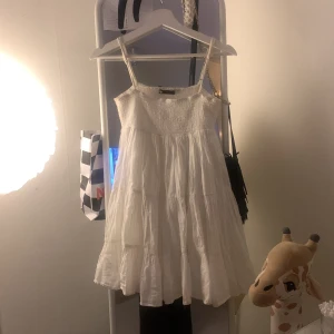 Vit klänning från Zara - Säljer en superfin vit klänning från Zara i storlek XS. Den är ärmlös och har en luftig passform, perfekt för sommardagar. Klänningen har en smockad överdel och volangdetaljer som ger en romantisk känsla. Tillverkad i ett lätt och bekvämt material.