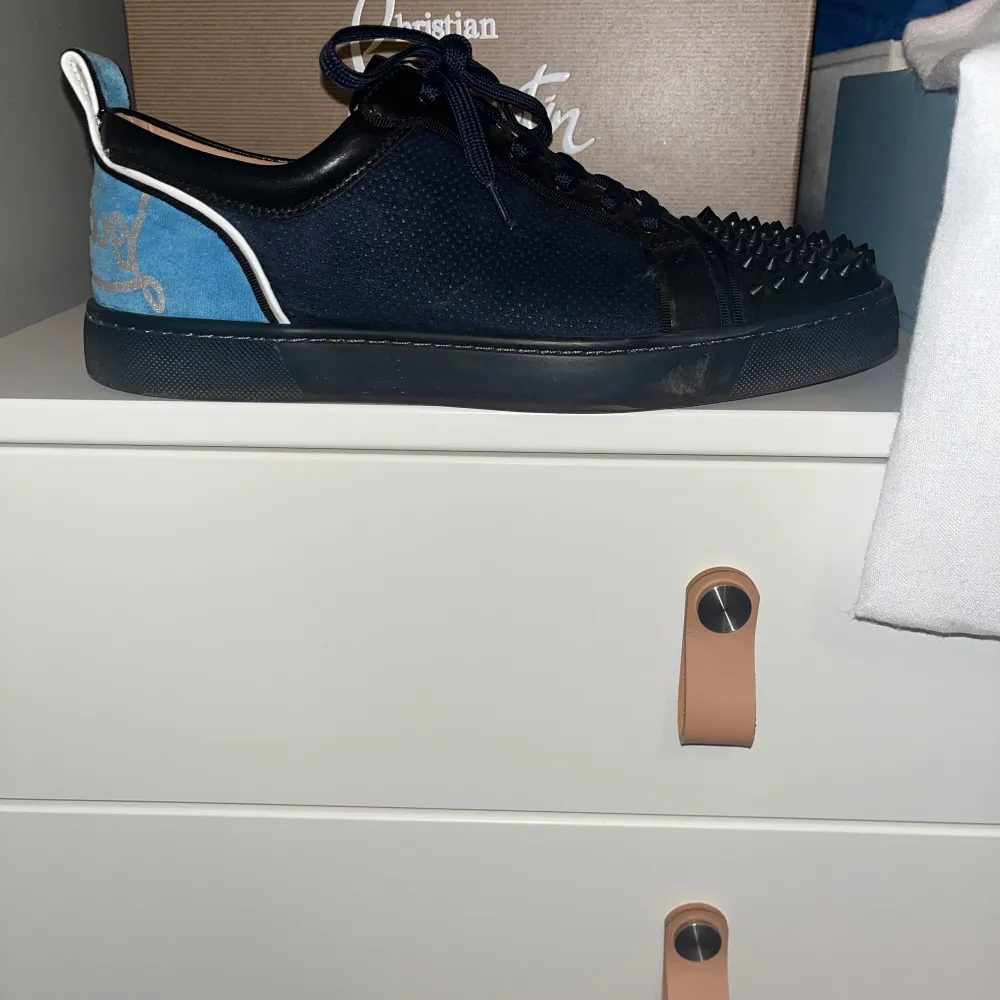 Säljer ett par blåa Christian Louboutin sneakers i mycket bra skick. Skorna har en cool design med svarta nitar på tån och en blå detalj på hälen. Kommer med originalförpackning och dustbag. Pris går att diskutera, SJÄLVA ÄKTA!. Skor.