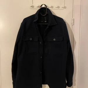 Mörkblå overshirt från 157 - Säljer en snygg mörkblå overshirt från 157 i bra skick. Den har långa ärmar och knappar framtill, perfekt för höst och vår. Stilren och enkel att matcha med olika outfits. Passar både till vardags och lite mer uppklädda tillfällen.