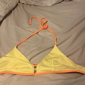 Gul och orange bikiniöverdel - Säljer en snygg gul bikiniöverdel med orangea detaljer och knytband. Perfekt för sommardagar på stranden eller vid poolen. Den har en enkel och stilren design med en bekväm passform. Använd ett fåtal gånger, så den är i mycket bra skick. Passa på att fynda denna färgglada överdel! 🌞
