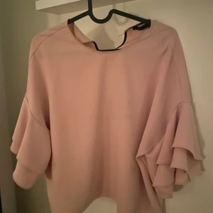 Rosa tröja med volangärmar från Zara - Säljer en superfin rosa tröja från Zara med volangärmar. Perfekt för att piffa upp vardagslooken eller till en festlig kväll. Tröjan har en lös passform och är i mycket bra skick. Passar perfekt till både jeans och kjol! Knappen där bak har lossnat men inget jag har märkt eller stört mig på 💕