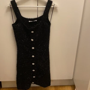 Svart glittrig klänning från Zara - Snygg svart glittrig klänning från Zara i storlek S. Klänningen har dekorativa knappar framtill och är perfekt för festliga tillfällen. Den är ärmlös och har en tight passform som framhäver figuren. Perfekt för en utekväll eller nyårsfest! Aldrig använd! 