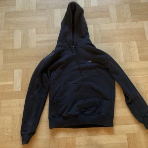 Svart hoodie från Ami - Säljer en svart hoodie från Ami, designad av Alexandre Mattiussi. Den har en klassisk passform med en praktisk ficka framtill och en justerbar huva. Lite slitage på ärmsluten men annars i bra skick.