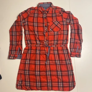 Rutig klänning från Tommy Hilfiger - Säljer en superfin rutig klänning från Tommy Hilfiger i rött, blått och vitt. Den har långa ärmar och knappar framtill, samt ett bälte i midjan för en snygg passform. Perfekt för höst och vår! 🧡