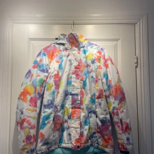 Skidjacka  - Säljer en supercool jacka med ett färgglatt mönster i rosa, blått, gult och orange. Jackan har en dragkedja och huva, perfekt för att lysa upp gråa dagar. Den är använd två skidsäsonger. 