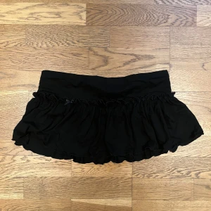 Svart volangkjol - Snygg svart kortkjol med volanger. Perfekt för att ge en extra touch till din outfit. Den har en elastisk midja för bekväm passform.