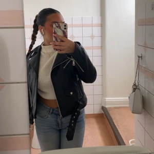 Svart skinnjacka med dragkedja - Snygg svart skinnjacka från ZARA med dragkedja och bälte. Perfekt för en cool outfit. Jackan har en klassisk bikerstil med flera dragkedjor och detaljer.