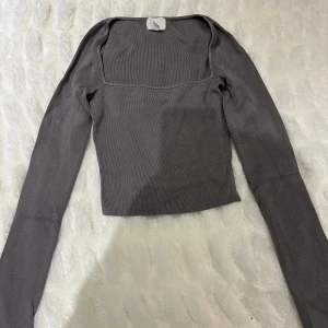 Grå ribbad topp - Snygg grå ribbad topp med långärmad design och fyrkantig halsringning. Perfekt för en stilren look. Passar bra till både jeans och kjol.