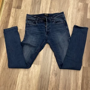 Mörkblå slim jeans från Jack & Jones - Snygga mörkblå slim jeans från Jack & Jones med klassisk femficksdesign. De har en knappgylf och är perfekta för en stilren look. Passar bra till både vardag och mer uppklädda tillfällen. Storlek 29/32