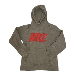 Grå Nike hoodie - Säljer en grå hoodie från Nike med en rosa logga på bröstet. Tröjan har långa ärmar och en klassisk huva. Perfekt för en avslappnad stil. Lite sliten dock.