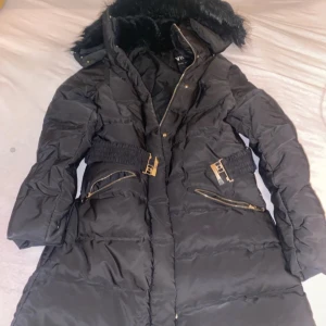 Svart dunjacka med pälskrage - Snygg svart dunjacka med pälskrage och dragkedjor. Jackan har långa ärmar och en figursydd passform med bältesdetaljer i midjan. Perfekt för kalla dagar. Från Zara! 