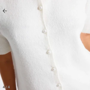 Vit kofta med pärlknappar - Säljer en stilren vit kofta med korta ärmar och dekorativa pärlknappar framtill. Perfekt för en elegant och avslappnad look. Passar bra till jeans eller kjol.