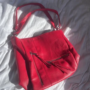 Röd axelväska i skinn - Snygg röd axelväska i skinn med flera dragkedjor och praktiska fack. Väskan har justerbara axelremmar och silverfärgade detaljer❤️❤️