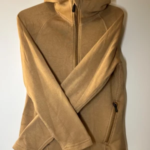 Beige fleecejacka med huva - Säljer en mysig beige fleecejacka med huva och dragkedja framtill. Jackan har långa ärmar och fickor med dragkedja på framsidan. Tröjan är lite ljusare i verkligheten. 