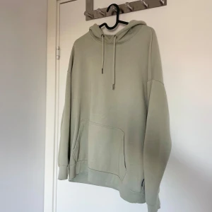 Grön hoodie med ficka - Säljer en stilren grön hoodie med stor ficka framtill och justerbar huva. Perfekt för en avslappnad look. Passar bra till både jeans och mjukisbyxor.