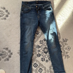Blå jeans från Jack & Jones - Snygga blå jeans från Jack & Jones med knappgylf och klassisk femficksdesign. Perfekta för en avslappnad stil. De har en normal passform och är tillverkade i slitstarkt denim. Slimfit!