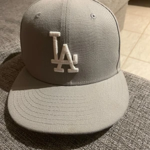 Grå keps från New Era - Snygg grå keps från New Era med LA-logga framtill. Tillverkad i 100% polyester och har en klassisk passform. Perfekt för att ge din outfit en sportig touch. 55,6cm 