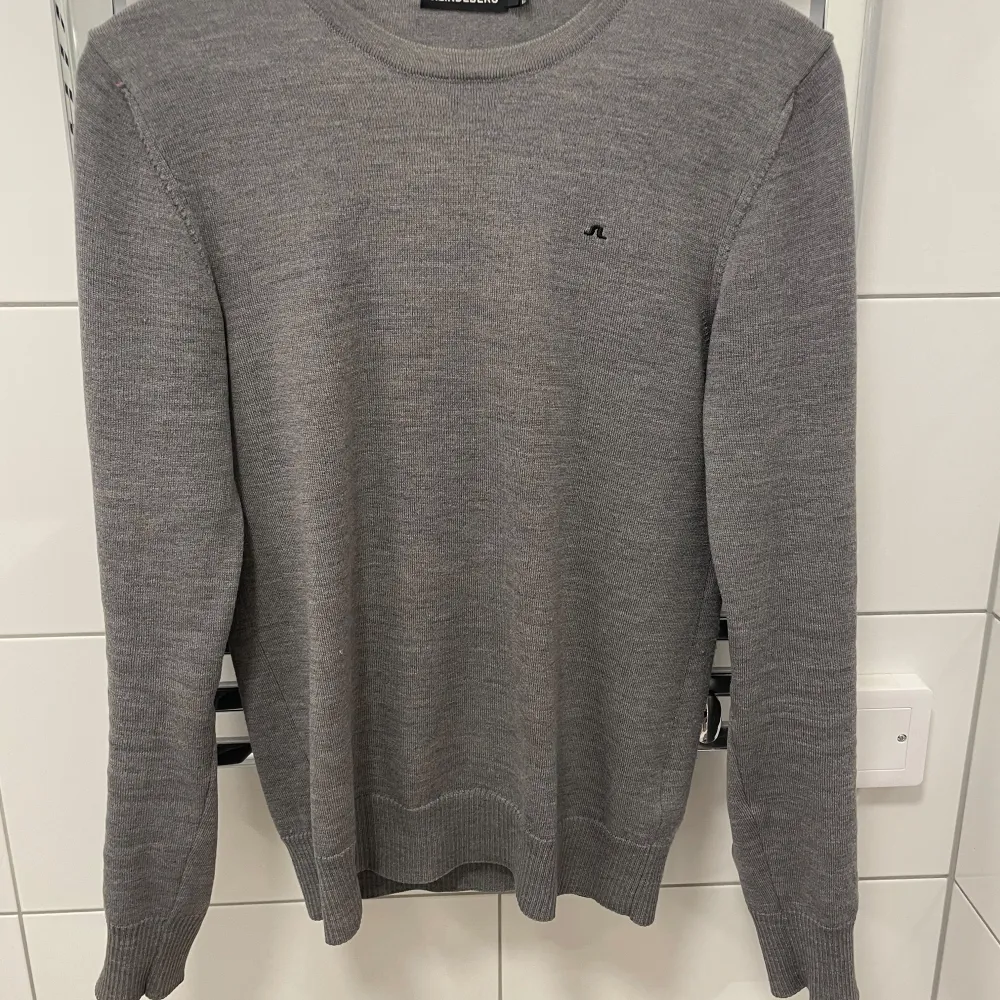 Snygg grå tröja från J. Lindeberg i 100% merinoull. Den har en klassisk rund hals och långa ärmar, perfekt för kyligare dagar. Diskret logga på bröstet ger en stilren look. Passar bra till både jeans och chinos. Köpt på emporia i Malmö . Neuletakit & Villapaidat.