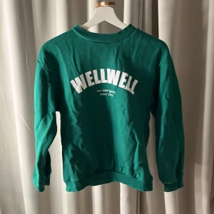 Grön sweatshirt från Wellwell - Säljer en grön sweatshirt från Wellwell med tryck framtill. Tröjan har långa ärmar och en rund halsringning. Perfekt för en avslappnad stil.