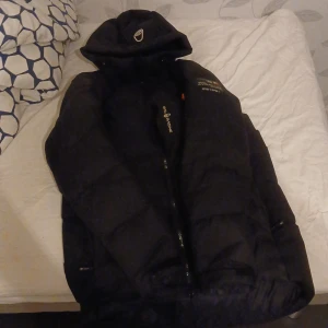 Svart dunjacka från Sail Racing - Säljer en svart dunjacka från Sail Racing med logotypen 'Sail Antarctica' på bröstet. Jackan har en dragkedja framtill och är långärmad. Perfekt för kalla dagar med sin varma och skyddande design. Storlek S men passar även M priset går att diskutera jackan har ett litet märke som knappt syns på armen som du ser på bilddn