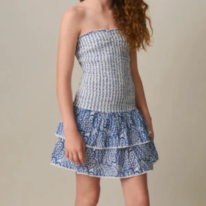 Blåvit axelbandslös klänning - Snygg sommarklänning klänning i blått och vitt med ett unikt mönster. Klänningen har en tight passform upptill och en volangkjol. Ny med prislapp kvar strl 158-164 men är stretchig nog för att passa xs-m