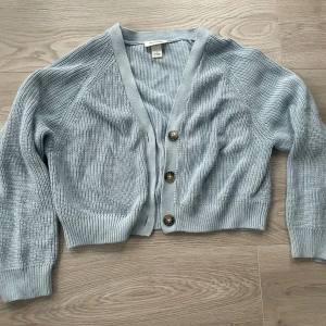 Ljusblå stickad kofta från Monki - Säljer en ljusblå stickad kofta från Monki med tre stora knappar framtill. Använd en visar inte några tydliga defekter💕