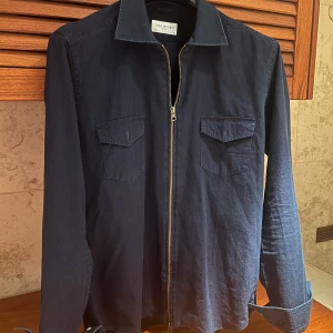 Mörkblå overshirt från John Henric - Snygg mörkblå overshirt från John Henric med dragkedja framtill och två bröstfickor. Perfekt för lager-på-lager-stil. Tillverkad i ett mjukt material som ger en bekväm passform. En stilren och mångsidig jacka för olika tillfällen. Size: medium