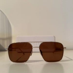 Chimi Aviator Solglasögon  - Snygga bruna solglasögon från Chimi med en stilren design. De har en fyrkantig form och tunna metallbågar som ger en modern look. Perfekta för soliga dagar och kommer med ett praktiskt fodral.