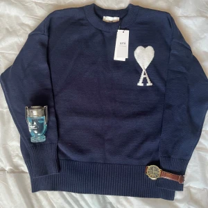 Ami Paris navy blue  - Säljer en snygg mörkblå tröja från Ami med ett vitt hjärta och bokstaven A på bröstet. Tröjan har långa ärmar och en rund halsringning. Perfekt för en stilren look.