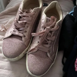 Rosa glittriga sneakers från Sprout - Snygga rosa sneakers från Sprout med glittrigt mönster och breda satinliknande skosnören. Perfekta för att ge lite extra bling till din outfit. Skorna har en bekväm platt sula och är i storlek 36.