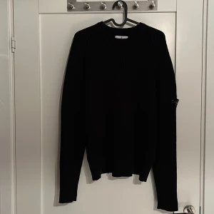 Svart stickad tröja från Stone Island - Säljer en stilren svart stickad tröja från Stone Island. . Perfekt för kyligare dagar och ger en snygg look och passar bra att ha under en väst. Skicket är bra på en del ställen är den en aning nopprig men inget man tänker på eller stör, varan är så klart äkta. Tröjan är i storlek 170cm men jag skulle säga att den passar xs/S. Vid snabb affär kan priset sänkas, Vid fler frågor eller funderingar är det bara att höra av sig/ Grischoutlet.