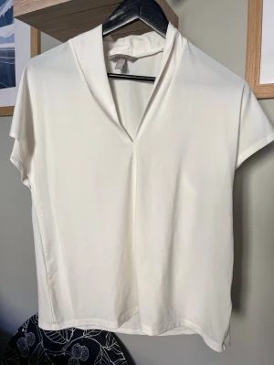 Vit v-ringad topp från H&M - Säljer en enkel och stilren vit topp från H&M med v-ringad hals och korta ärmar. Toppen har en mjuk och lätt känsla, perfekt till många olika outfits. Passformen är normal och materialet känns lent mot huden.