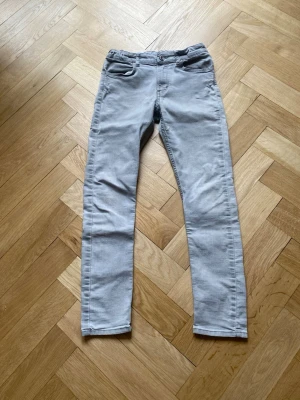 Ljusgråa slim fit jeans - Säljer ett par ljusgråa slim fit jeans med klassisk femficksdesign och normal midja. Jeansen har raka ben och stängs med knapp och dragkedja. Perfekta för dig som gillar en enkel och stilren look.